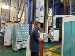 A skilled technician in protective gear operating a CNC touchscreen control panel for automated aluminum surface treatment at the factory.