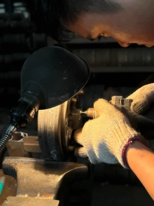 Close-up of a skilled machinist carefully grinding and polishing a custom metal die component under a work lamp.